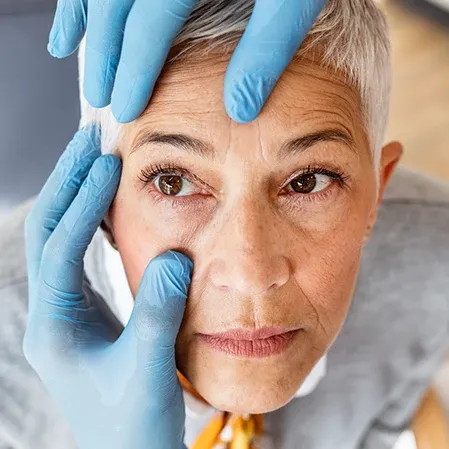 A close-up of a healthcare professional wearing blue gloves performing an eye check, indicating a precise diagnostic procedure.
